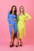 two stylish sexy attractive women posing full height on pink background in stylish colorful dresses of blue and yellow color, spring fashion trend photo