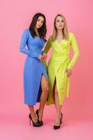 two stylish sexy attractive women posing full height on pink background in stylish colorful dresses of blue and yellow color, spring fashion trend photo