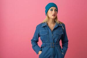 excited attractive girl posing on pink background in denim overall fashion trend photo