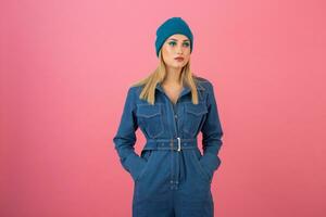 excited attractive girl posing on pink background in denim overall fashion trend photo