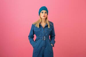 excited attractive girl posing on pink background in denim overall fashion trend photo