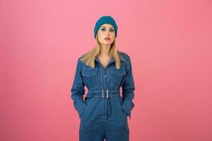 excited attractive girl posing on pink background in denim overall fashion trend photo