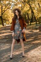 attractive stylish woman walking in park dressed in warm brown coat photo