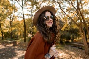 attractive stylish woman walking in park dressed in warm brown coat photo