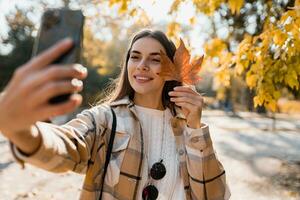 attractive young woman walking in autumn wearing jacket using phone photo