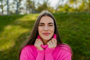 young smiling woman in pink sweater walking in green park photo