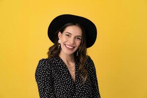 attractive woman posing isolated on yellow background wearing black hat and dress photo