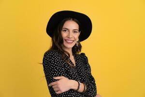 attractive woman posing isolated on yellow background wearing black hat and dress photo