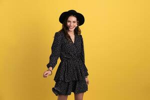 attractive woman posing isolated on yellow background wearing black hat and dress photo