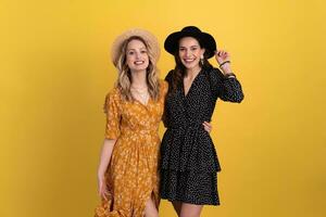 beautiful women friends together isolated on yellow background in black and yellow dress and hat photo