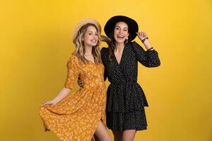 beautiful women friends together isolated on yellow background in black and yellow dress and hat photo