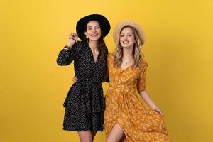 beautiful women friends together isolated on yellow background in black and yellow dress and hat photo