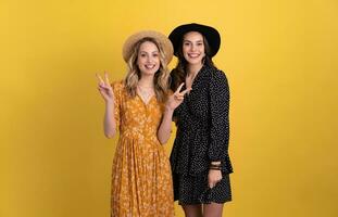 beautiful women friends together isolated on yellow background in black and yellow dress and hat photo