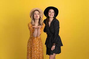 beautiful women friends together isolated on yellow background in black and yellow dress and hat photo