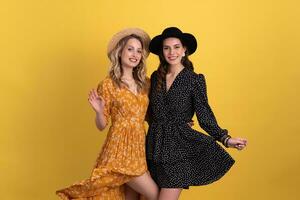 beautiful women friends together isolated on yellow background in black and yellow dress and hat photo