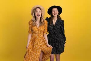 beautiful women friends together isolated on yellow background in black and yellow dress and hat photo