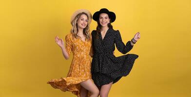 beautiful women friends together isolated on yellow background in black and yellow dress and hat photo