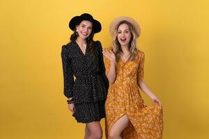 beautiful women friends together isolated on yellow background in black and yellow dress and hat photo