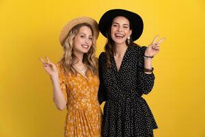 beautiful women friends together isolated on yellow background in black and yellow dress and hat photo