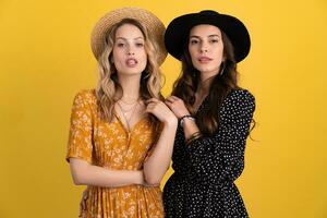 beautiful women friends together isolated on yellow background in black and yellow dress and hat photo