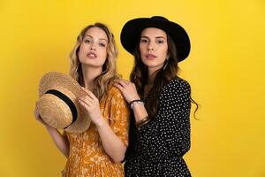 beautiful women friends together isolated on yellow background in black and yellow dress and hat photo