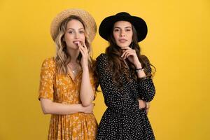 beautiful women friends together isolated on yellow background in black and yellow dress and hat photo