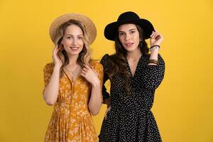 beautiful women friends together isolated on yellow background in black and yellow dress and hat photo