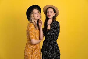 beautiful women friends together isolated on yellow background in black and yellow dress and hat photo