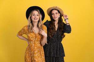 beautiful women friends together isolated on yellow background in black and yellow dress and hat photo