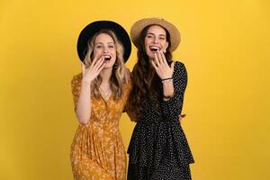 beautiful women friends together isolated on yellow background in black and yellow dress and hat photo