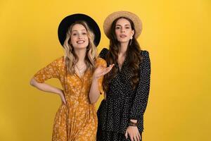 beautiful women friends together isolated on yellow background in black and yellow dress and hat photo