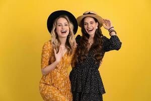 beautiful women friends together isolated on yellow background in black and yellow dress and hat photo