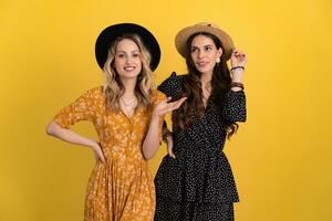 beautiful women friends together isolated on yellow background in black and yellow dress and hat photo