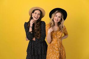 beautiful women friends together isolated on yellow background in black and yellow dress and hat photo