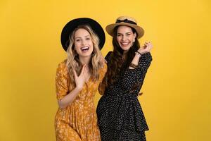 beautiful women friends together isolated on yellow background in black and yellow dress and hat photo