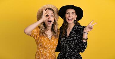 beautiful women friends together isolated on yellow background in black and yellow dress and hat photo