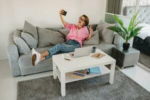 atractivo sonriente mujer en rosado camisa sentado relajado en sofá a hogar foto