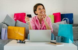 happy smiling woman in pink shirt on sofa at home shopping online photo