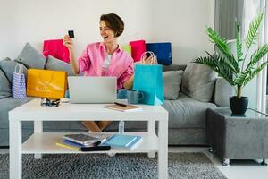happy smiling woman in pink shirt on sofa at home shopping online photo