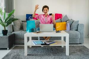 contento sonriente mujer en rosado camisa en sofá a hogar compras en línea foto