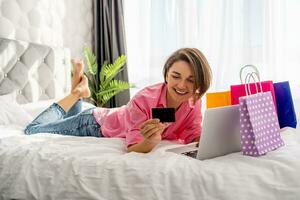 bonito contento mujer acostado en cama a hogar compras en línea foto