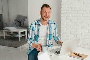 man in shirt sitting in kitchen at home at table working online on laptop photo