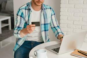 man in shirt sitting in kitchen at home at table working online on laptop photo