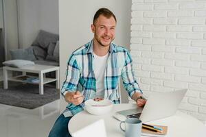 man in shirt sitting in kitchen at home at table working online on laptop photo