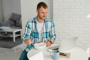 man in shirt sitting in kitchen at home at table working online on laptop photo