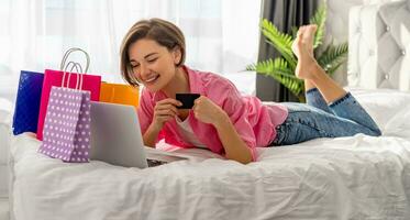 pretty happy woman lying on bed at home shopping online photo