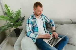 handsome busy focused man in shirt sitting relaxed on sofa at home at table working online photo