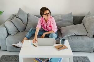 woman in pink shirt sitting relaxed on sofa at home at table working online on laptop photo