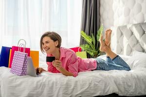 pretty happy woman lying on bed at home shopping online photo