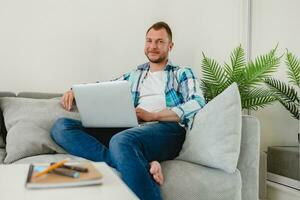 handsome busy focused man in shirt sitting relaxed on sofa at home at table working online photo